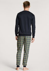 Haut à manches longues marine avec un pantalon à carreaux assorti en bleu, jaune et blanc. Le pantalon possède des poignets élastiques et une coupe décontractée.