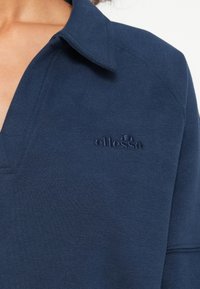 Navy blauwe trui met een kraag, gemaakt van gestructureerde stof. Bevat een geborduurd logo op de borst en heeft een ontspannen pasvorm.
