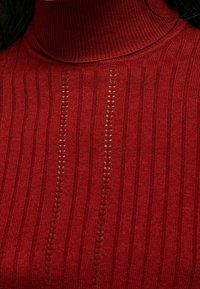 Haut rouge à col roulé côtelé présentant des lignes verticales et des accents en tricot ajouré, fabriqué dans un matériau doux et texturé.