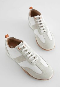 Weiße und hellgraue Sneakers aus Leder und Wildleder mit einer runden Zehenkappe, weißen Schnürsenkeln und einer braunen Gummisohle mit Akzentstreifen.