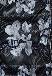 Sort quiltet stof med et blomstermønster i nuancer af blå og hvid. Indeholder "Armani Jeans"-logoer som accenter.