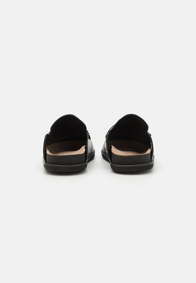 Sandali slip-on neri in pelle con retro aperto, suole piatte e solette di un beige chiaro. Presentano dettagli testurizzati sottili sulla tomaia.