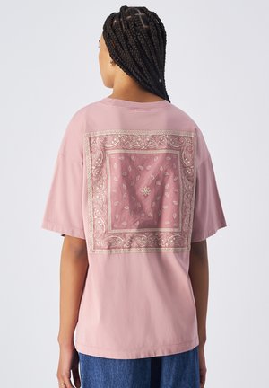 Camiseta de algodón rosa con un estampado decorativo estilo bandana en dorado en la parte posterior, de corte amplio y mangas cortas.