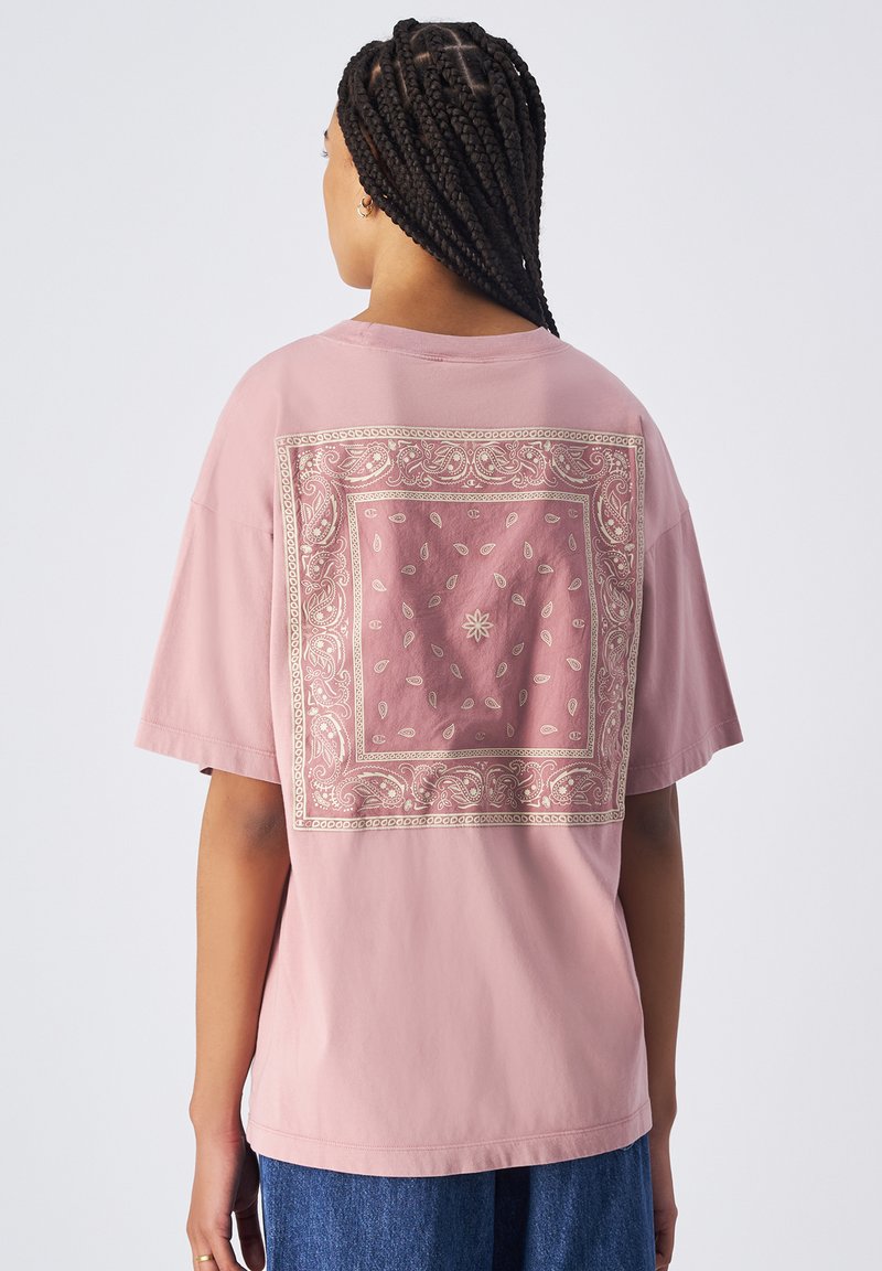 Camiseta de algodón rosa con un estampado decorativo estilo bandana en dorado en la parte posterior, de corte amplio y mangas cortas.