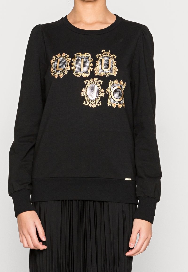 Sudadera negra con diseños gráficos ornamentados en dorado y cuadros. Cuello redondo clásico con mangas abullonadas, confeccionada en tela suave.