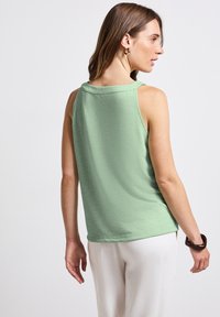Bledě zelená bezramínková blůza s volným střihem, která má měkkou strukturu a skromný výstřih na zádech. Nosit s kalhotami světlé barvy.