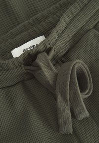 Olivgrüne Shorts aus strukturiertem Waffelstrickstoff. Mit einem verstellbaren Kordelzug in der Taille und einem sichtbaren Markenlabel mit der Aufschrift "GABBA".