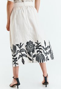 Linned midi-nederdel i lys beige med sorte blomster- og bladmønstre i kanten. Kombineret med sorte, strop sandaler med hæl.