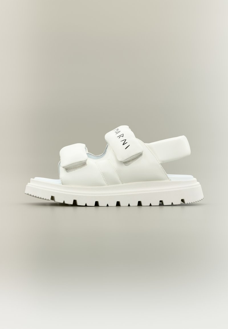 Λευκά δερμάτινα σανδάλια με επίπεδη, χοντρή σόλα. Διαθέτουν δύο επενδυμένες λουρίδες και ρυθμιζόμενο πίσω λουρί. Μινιμαλιστικός σχεδιασμός με διακριτικές λεπτομέρειες επωνυμίας.