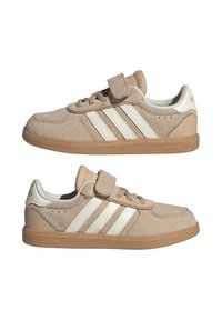 Baskets Adidas en daim beige avec des bandes blanches, semelles en gomme, lacets et une bride Velcro sur le dessus, vues des deux côtés.