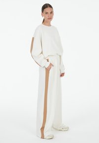 White oversized sweatshirt with tan side stripes, paired with matching wide-leg pants featuring a pocket. Smooth texture and relaxed fit.