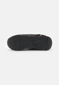 Suela de zapato de goma negra con patrón de agarre circular y nombre de marca en relieve. Presenta secciones elevadas para tracción. Diseño plano y ancho.