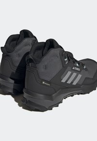 Chaussures de randonnée Adidas Terrex noires et grises avec tissu Gore-Tex, semelles robustes et fermeture à lacets, vue latérale et arrière en angle sur un fond clair.