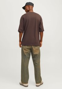 Løs siddende brun t-shirt med korte ærmer, parret med falmede grønne bukser med vidde. Kompleteret med en marineblå kasket og lyse sandaler.