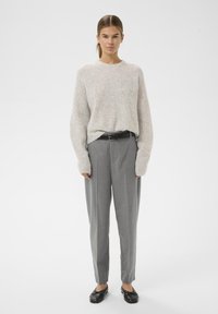 Maglione grigio chiaro, texture, con maniche ampie abbinato a pantaloni grigi a righe. Una cintura nera e scarpe nere piatte completano il look.