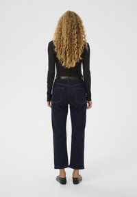 Tumedad sinises denim püksid otsekärpimisega, nähtavate õmblustega ja kahe tagataskuga, kombinatsioonis sobitatud musta pika varrukaga topiga.