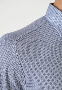 Blau gemustertes Hemd mit geometrischem Design und strukturierter Oberfläche. Der Kragen ist strukturiert und aus glattem Stoff gefertigt.