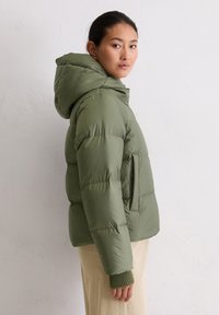 Kurtka puchowa w oliwkowej zieleni z kapturem, posiadająca pikowane części i boczną kieszeń, zestawiona z ściągaczami na rękawach oraz neutralnym dołem.