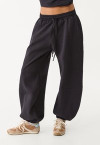 Zwarte relax-fit sweatpants met een elastische tailleband, zijzakken en een boordafwerking, gecombineerd met beige en bruine sportschoenen.
