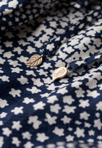 Tejido azul marino con patrón floral blanco; incluye etiquetas ovaladas y de hojas de plata con la marca 'Superdry'; textura suave.