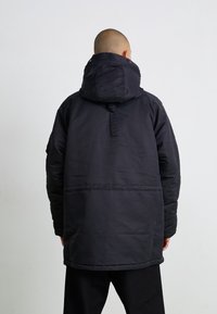 Zwarte geïsoleerde jas met capuchon, met een gladde textuur, verstelbare halslijn en een naad over het midden.