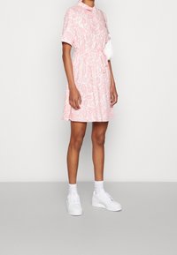 Vestido de estampado paisley en tonos rosas con mangas cortas, cuello tipo polo, cintura ceñida y falda acampanada. Combinado con zapatillas blancas y calcetines.