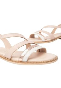 Sandali in pelle beige con cinghie incrociate, caratterizzati da un accento metallico argento. Suola piatta con una base in marrone chiaro texturizzata.