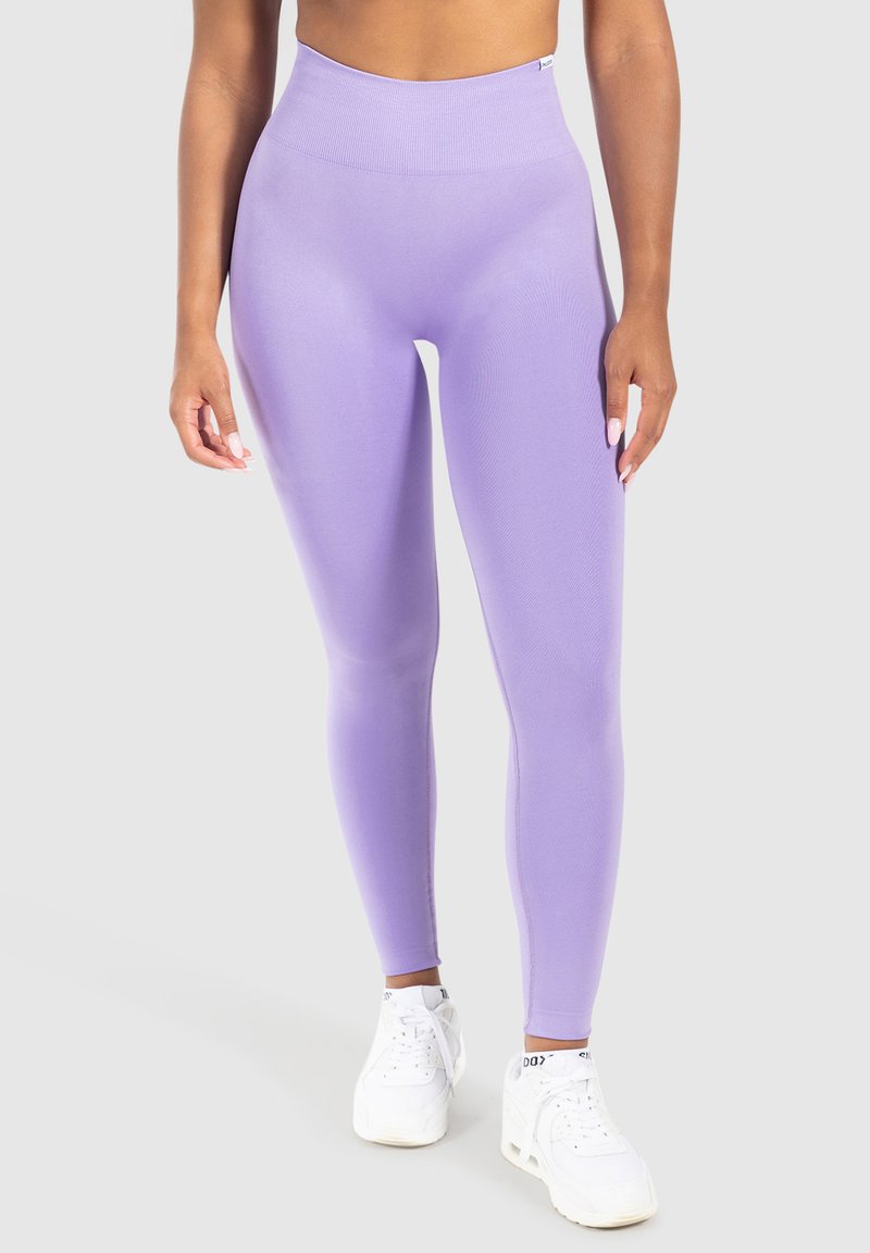 Leggings taille haute lavande fabriqués en tissu extensible avec une texture lisse. Associés à des chaussures de sport blanches. Design simple, sans motifs.