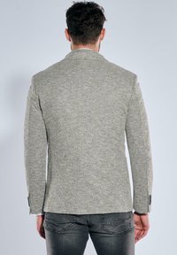 Gray textured blazer with a fitted design, single vent at the back, and buttoned cuffs. Paired with dark jeans.