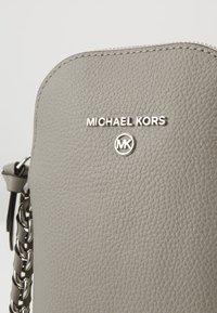 Nära bild av texturerad grå läder Michael Kors-väska fram med silverkedjesläp och silverlogotyp.