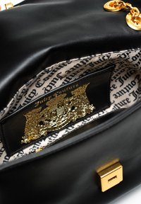 Interno di una borsa a tracolla in pelle nera, caratterizzato da un emblematic oro e una fodera con un motivo testuale. Include una chiusura metallica e dettagli di cucitura.
