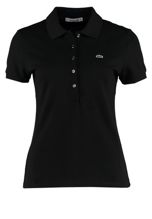 Personne marchant portant un polo noir à manches courtes, un jean bleu délavé avec des revers, et des chaussures blanches avec des embouts gris clair.