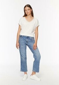 Witte korte mouwen V-hals t-shirt gecombineerd met lichtblauwe rechte jeans. Model draagt witte sneakers met zilveren accenten. Eenvoudige, casual outfit.