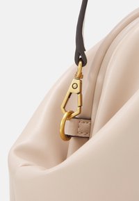 Beige læder håndtaske hjørne med en guld hardwarelås og en mørk læderrem. Blød tekstur og glat finish.