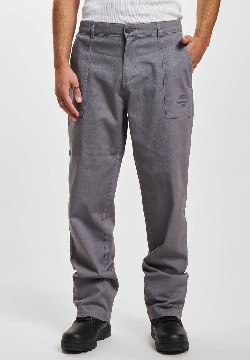 Szare bawełniane spodnie o luźnym kroju, z dwiema bocznymi kieszeniami, z zapięciem na guzik oraz szczegółami logo w pobliżu kieszeni. Czarne buty dopełniają outfit.