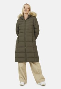 Cappotto imbottito verde oliva con cappuccio foderato in pelliccia, dotato di zip anteriore, tasche laterali e design lungo fino al ginocchio. Il tessuto ha una trama visibile.