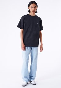 Sort bomulds T-shirt med rund halsudskæring og korte ærmer, parret med lyseblå denimjeans. Bemærkelsesværdigt lille logo på brystet.