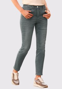 Graue Jeans aus Denim mit tailliertem Schnitt, ausgestattet mit Fronttaschen und Knopfverschluss; kombiniert mit beigen und braunen Sportschuhen.