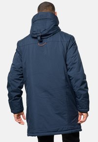 Parka isolée bleu marine avec col montant, capuche à cordon de serrage et fermeture ajustable. Texture lisse et détails cousus sur les manches.