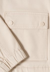 Beige stoffen jaszak met twee beige drukknoopjes met het label "CECIL" en een mouw met elastische boord.