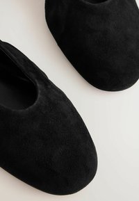 Černé semišové nazouvací boty s kulatou špičkou a hladkým vnitřním podšitím. Bez viditelného kovového příslušenství nebo vzorů.