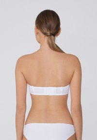 Bílá podprsenka bez ramínek s hladkým materiálem, elastickým páskem a zapínáním na háček a oko vzadu, s bezšvovým designem a neviditelnými ramínky.