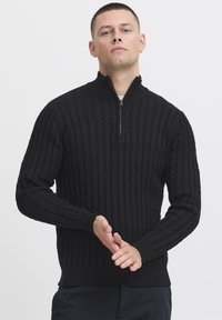 Zwarte gebreide trui met een ritssluiting bij de hoge kraag, textuur in kabelpatroon en geribde boorden en zoom. Geschikt voor casual kleding.