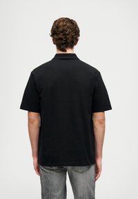 Svart kortärmad piké med klassisk krage. Slät tyget och avslappnad passform. Bakdelen har en ren, enkel design.