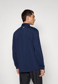 Polo-shirt à manches longues bleu marine avec un col, texture lisse et un petit logo au dos du cou. Offre une coupe décontractée et un ourlet droit.