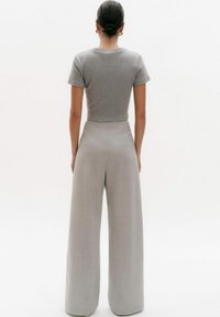 Szara dopasowana koszulka z krótkim rękawem w połączeniu z wysokim stanem, szerokimi, jasnoszarymi spodniami, które prezentują gładką, teksturowaną tkaninę.
