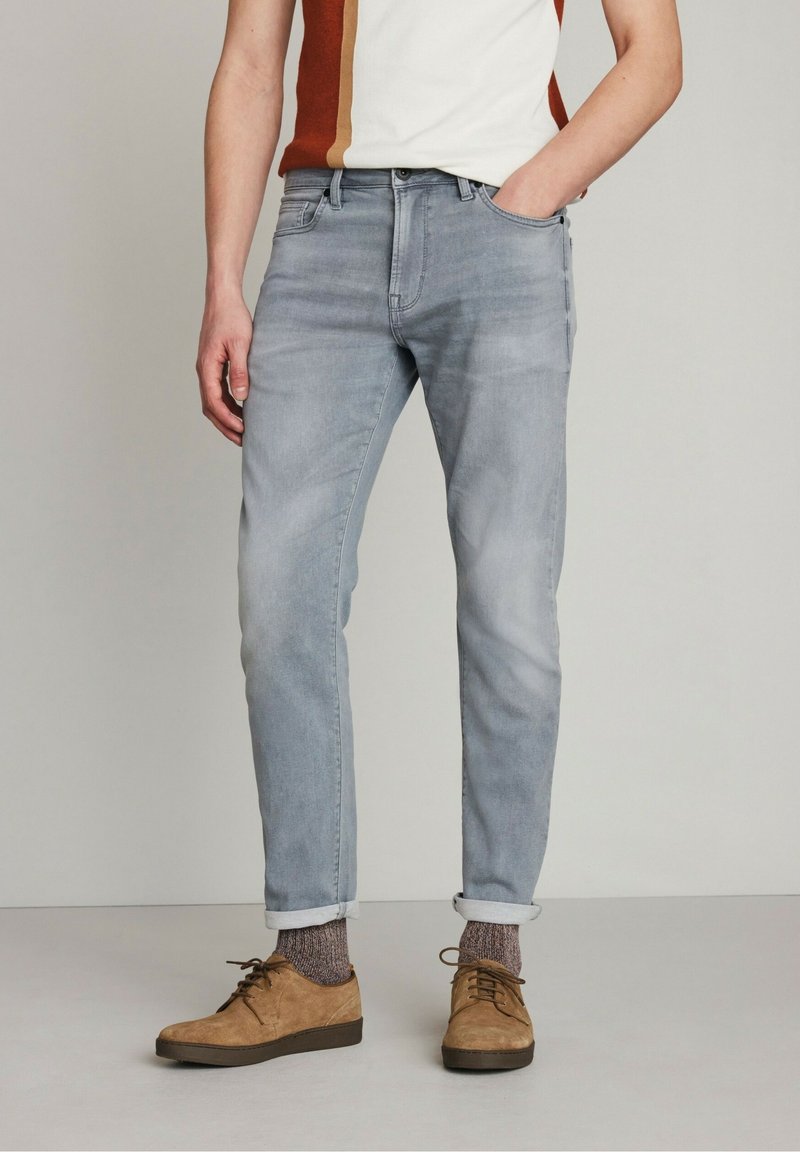 Jeans de mezclilla azul claro con un ajuste relajado, con los puños doblados en los tobillos. Llevados con zapatos de ante marrones y calcetines con estampado.