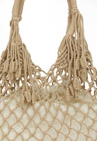 Beige bomulds tote taske med netdesign, flettede håndtag og dekorative kvaster. Indersiden har en samlet stofforet.