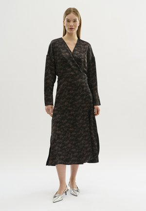Rochie neagră, tip wrap, cu un model abstract subtil în nuanțe de maro, mâneci lungi și o fanta pe lateral, asortată cu pantofi cu vârf ascuțit argintii.