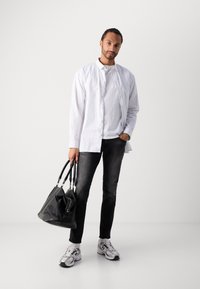 Cămașă albă cu dungi, tricou alb dedesubt, blugi negri, geantă neagră, adidași gri cu accente albe. Textură netedă, design casual.